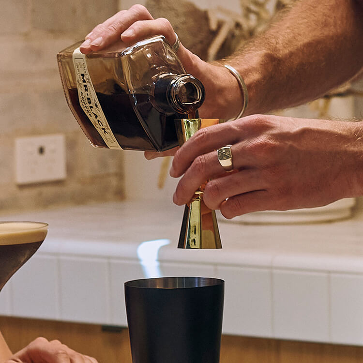 A person pouring Mr Black Cold Brew Coffee Liqueur into a cocktail jigger.